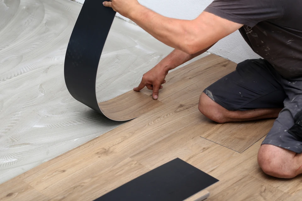 Artisan à genoux pose un revêtement de sol vinyle imitation bois dans un intérieur résidentiel
