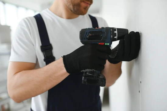 Professionnel installant un rail métallique au plafond à l'aide d'une perceuse-visseuse électrique turquoise