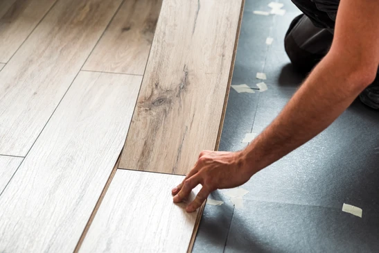 Intérieur d'habitation où un artisan en gants blancs installe du parquet flottant sur sous-couche