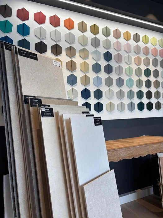 Showroom de carrelage avec mur d'exposition présentant des échantillons hexagonaux dans une large palette chromatique : teintes neutres, marines, pastels et vives