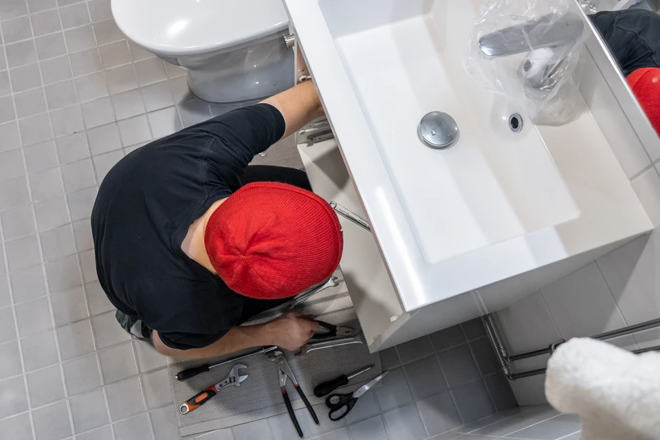 Plombier professionnel en salopette noire et t-shirt bleu installant une cabine de douche vitrée dans une salle de bains moderne carrelée